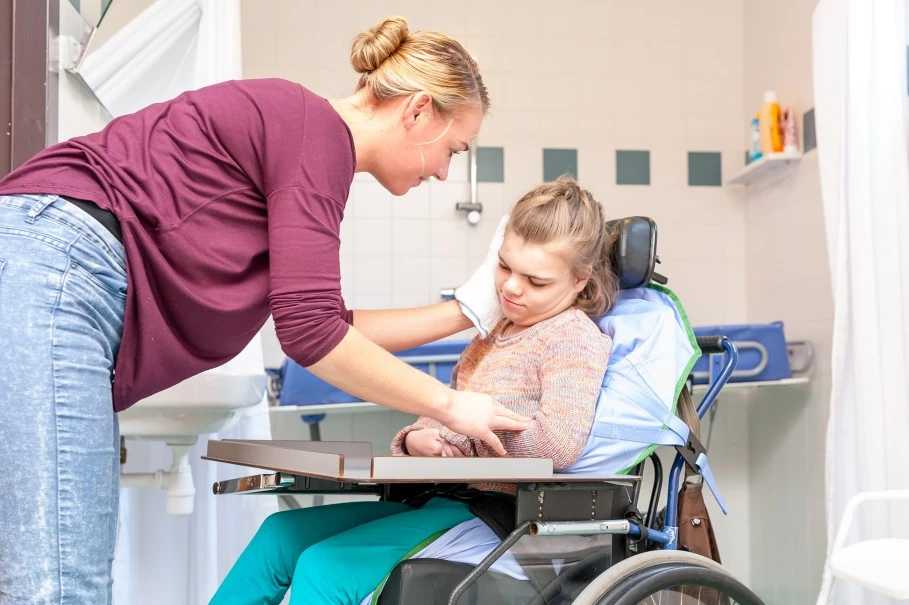 Support worker wiping face of disabled girl in wheelchair