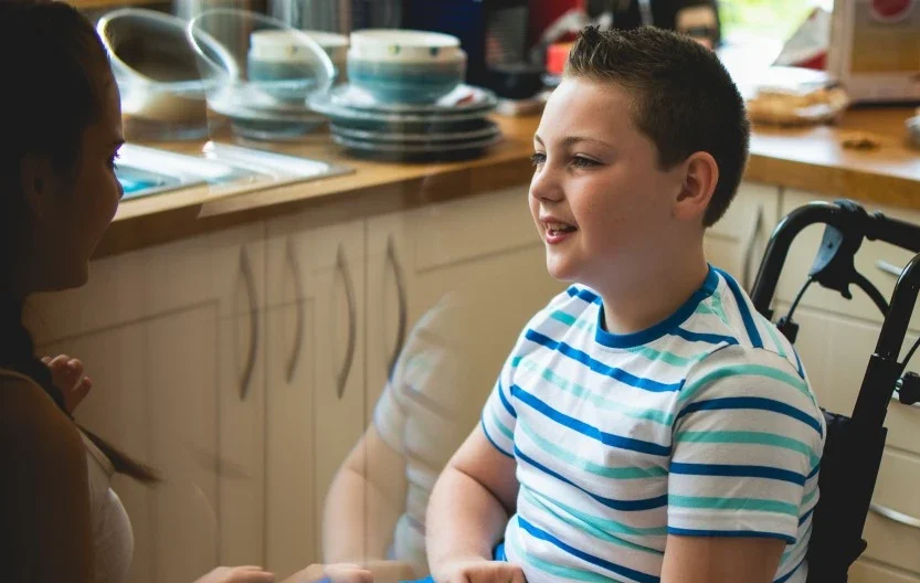 Disabled boy in wheelchair sitting in kitchen talking with support worker